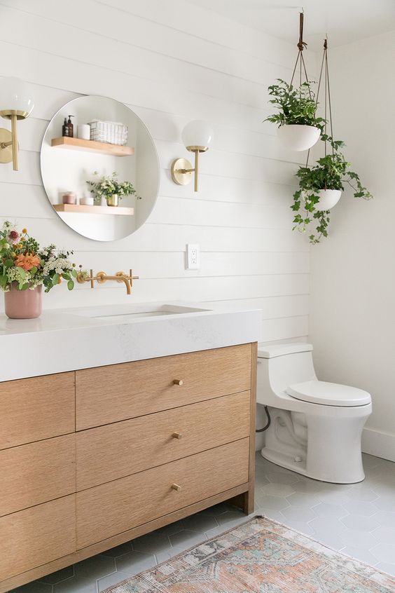 an airy contemporary meets boho bathroom with white shiplap, a light stained vanity, potted greenery and a round mirror