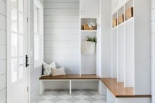 an airy mudroom with dove grey shiplap walls, a large storage unit with cabinets and open shelving, elegant glass lamps