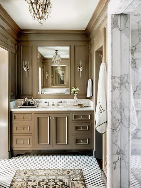 an elegant and refined taupe bathroom with a built in vanity, a mirror, sconces and a crystal chandelier plus a white marble shower