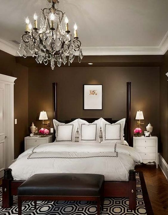 an elegant taupe bedroom with a black bed with pillars, white bedding, white nightstands, a chic crystal chandelier
