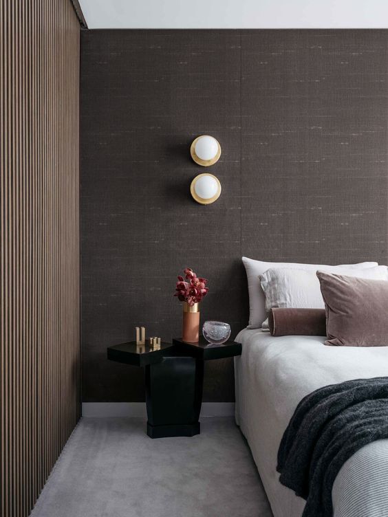 an exquisite bedroom with taupe fabric walls, a wooden slab wall, a neutral bed with neutral bedding, a catchy black nightstand