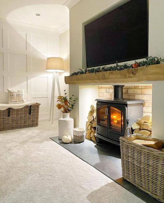 an inviting space with a wood burning stove, a mantel with greenery and a TV over it, baskets with firewood and more firewood stored on both sides of the fireplace