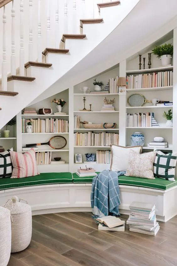 a cozy and stylish reading nook under the stairs, with built in bookshelves and a curved upholstered bench with lots of pillows