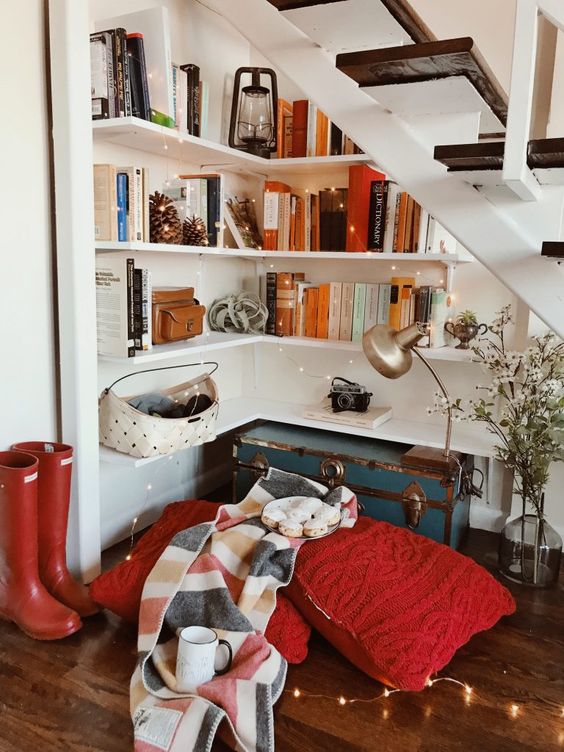 a fab reading nook under the stairs with corner shelves, lights, a vintage chest for storage, large pillows and blankets