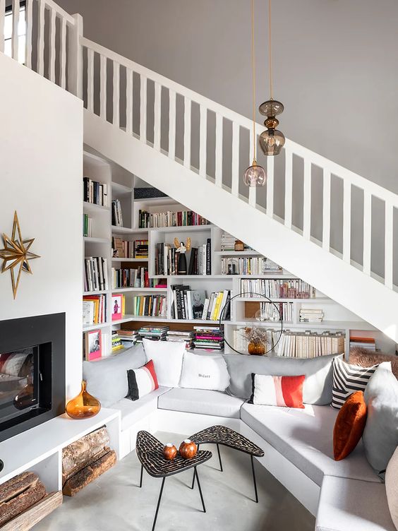 a gorgeous reading and sitting nook under the stairs, with lots of bookshelves, a geometric sectional sofa and a fireplace is amazing