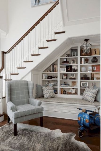 a lovely neutral reading nook with built-in shelves udner the stairs, a comfy daybed plus an additional wingback chair