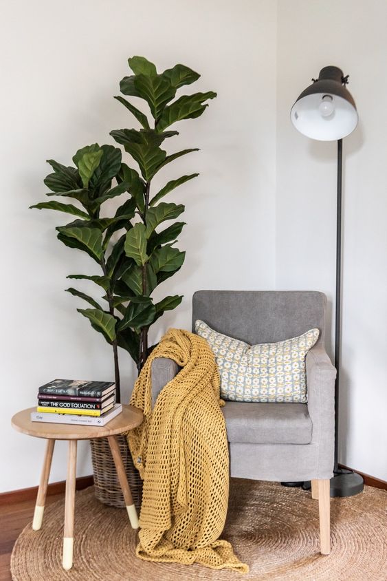 a lovely modern sitting nook with a grey chair, a pillow and a blanket, a floor lamp, a potted plant and a small coffee table