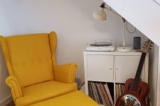 09 a small and stylish reading corner under the stairs, with a chic vinyl cabinet, a guitar and a mustard chair with a footrest