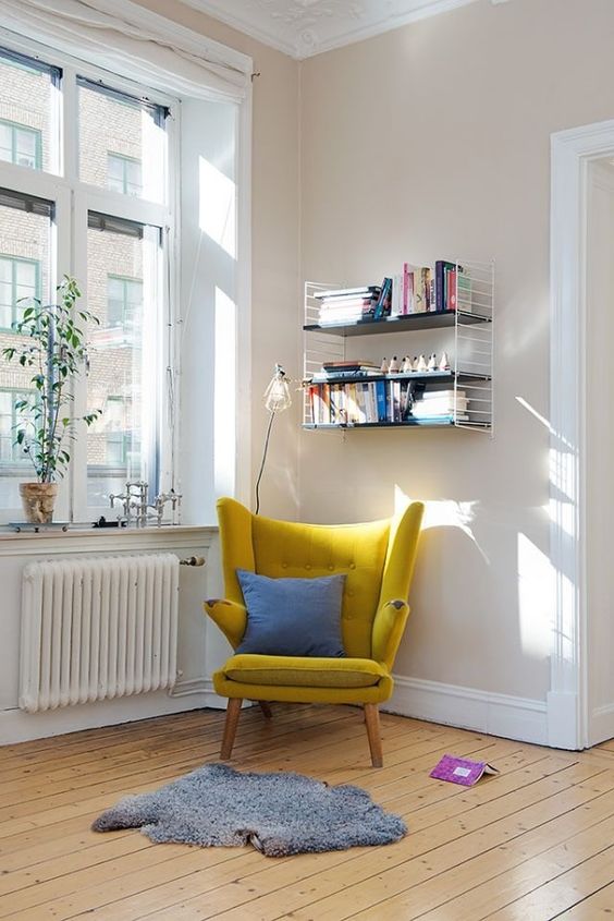 a welcoming reading space with a mustard wingback chair, a bookshelf, a rug and some greenery on the windowsill