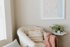 10 a small and lovely reading nook with a creamy chair, a couple of pillows and a blanket, a beach artwork, a small table and a faux fur rug