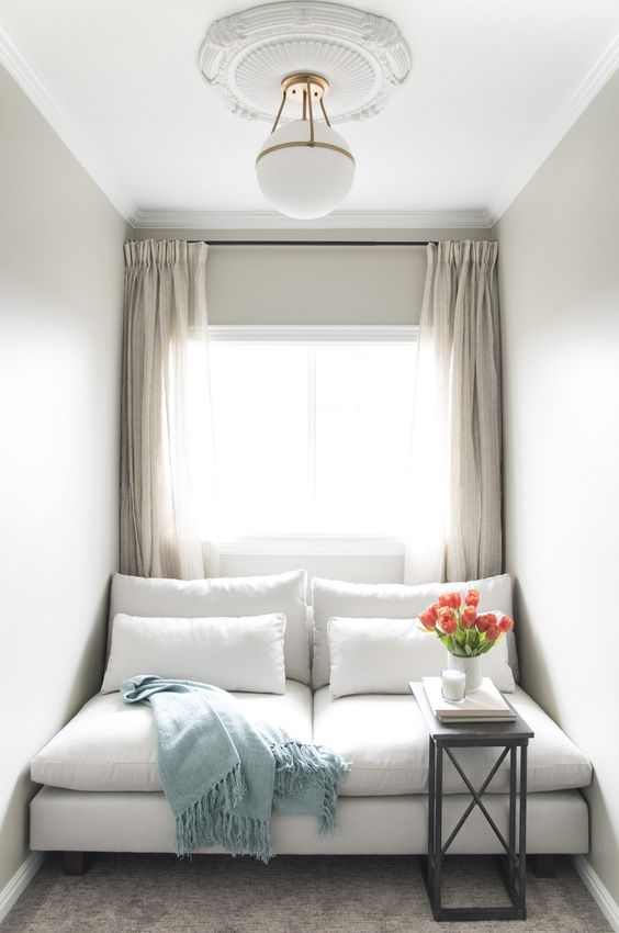 a modern neutral window nook styled with a daybed and pillows, with a small black coffee table and neutral curtains