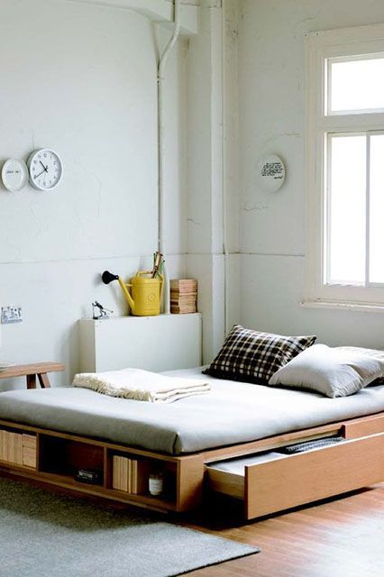 a modern light-filled bedroom with a bed with drawers and open storage compartments, a bench and cool white clocks