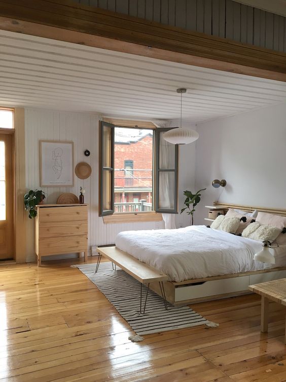 a Scandi bedroom with a light-stained bed with storage drawers, a planked headboard, a hairpin leg bench and stained chairs