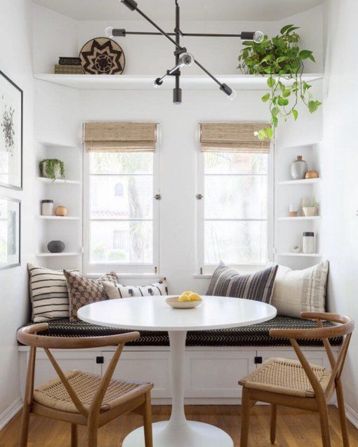 a small dining space with a built in windowsill bench, built in shelves, a round table and a couple of woven chairs