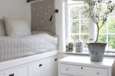 28 a lovely white cottage bedroom with a bed placed on a large storage unit, a dresser as a nightstand and grey textiles