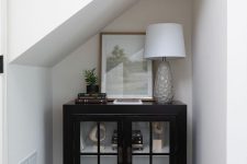28 a small awkward nook with an elegant black cabinet for storage and displaying, with a chic lamp and an artwork