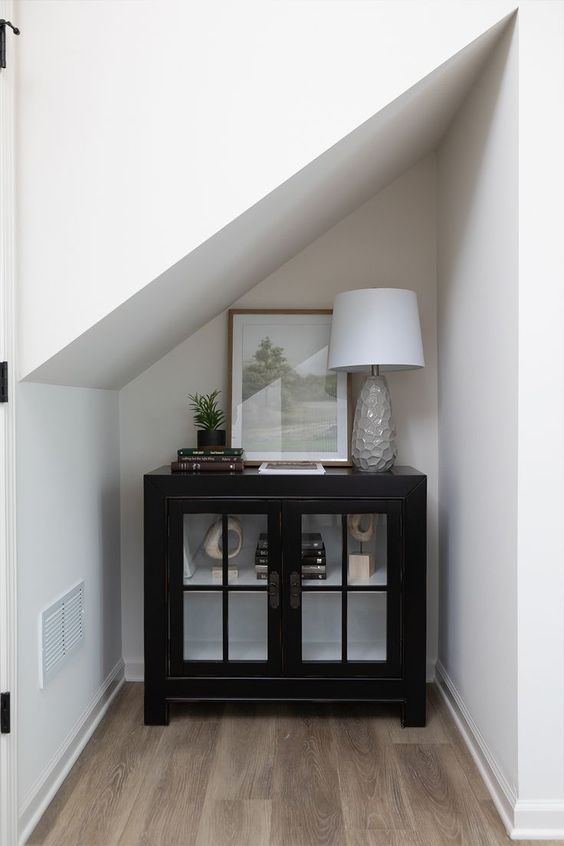 a small awkward nook with an elegant black cabinet for storage and displaying, with a chic lamp and an artwork