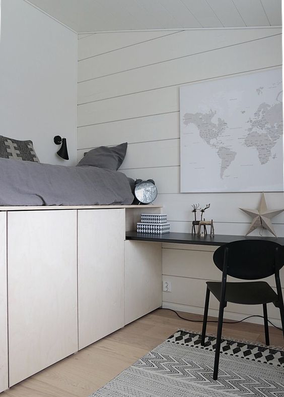 a neutral bedroom with a planked wall a bed placed on storage cabinets and a built in black desk and a chair