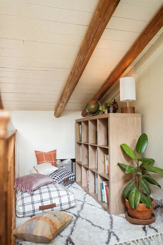 an attic nook taken by a bookshelf lots of cushions and pillows potted plants and a chic lamp for reading and just relaxing here