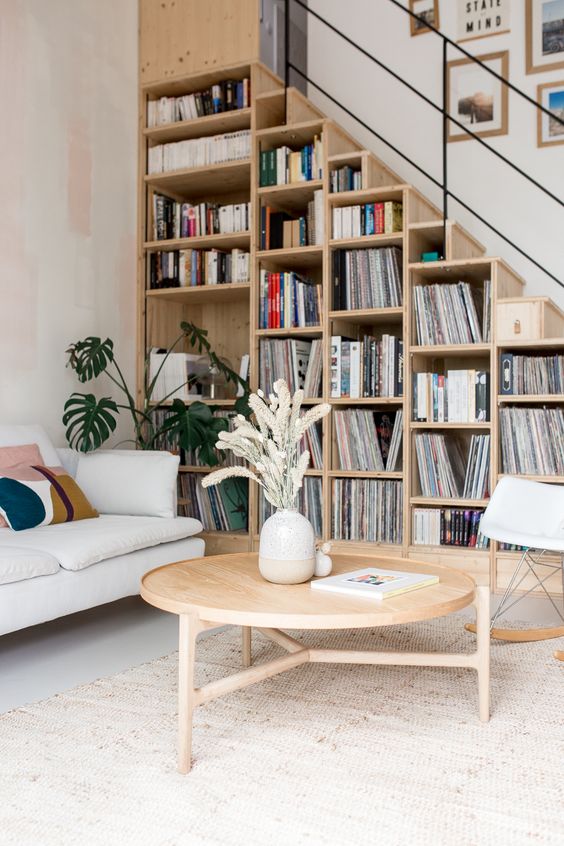 a stylish mid-century modern space with a bookcase staricase, a sofa, a round table and a comfy chair is very chic and practical