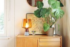 37 an awkward nook used for storage with a light-stained sideboard, a chic lamp, a potted plant and a map as an artwork