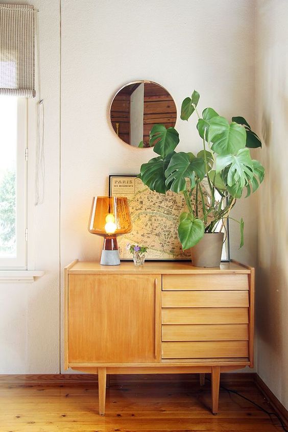 an awkward nook used for storage with a light-stained sideboard, a chic lamp, a potted plant and a map as an artwork