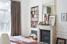 a French chic bedroom with paneling, an antique non-working fireplace, a bed with pink bedding, built-in shelves and a mirror