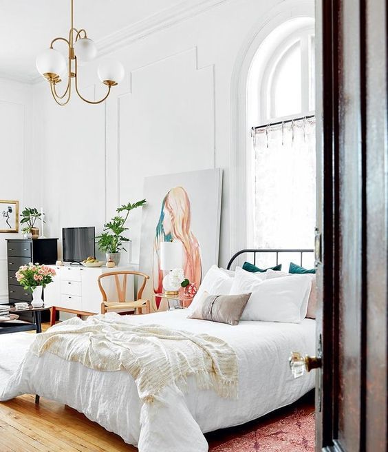 a French style bedroom with a metal bed with neutral bedding, a pink rug, stained and painted furniture and a statement artwork