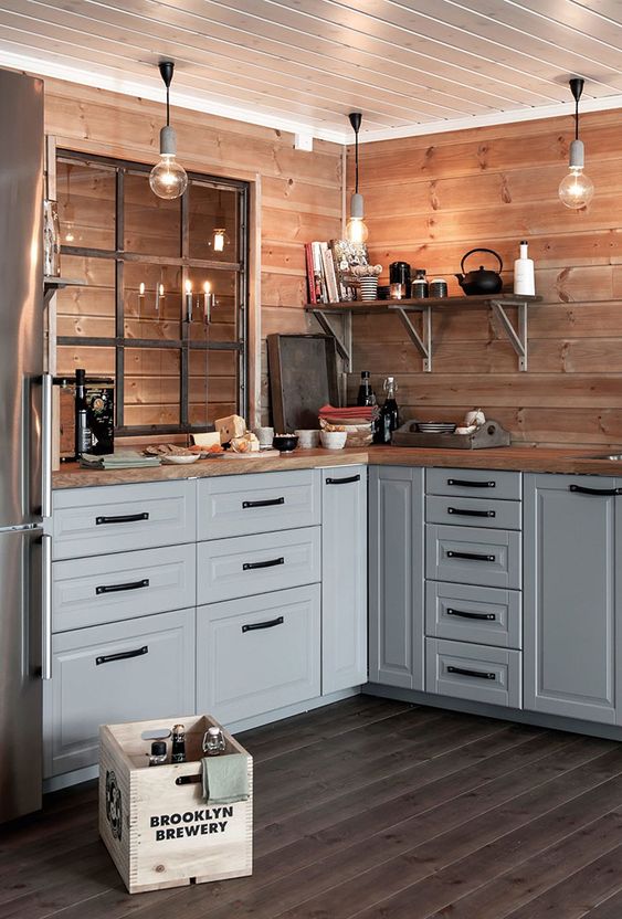 a Scandinavian kitchen with blonde wood planked walls, matching countertops, grey wooden cabinets and a planked wood floor of a greyish tone
