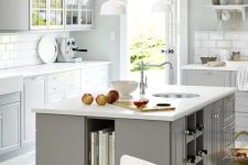 a Scandinavian kitchen with dove grey cabinets, white countertops and a white tile backsplash, a grey kitchen island with open book and wine bottle storage and drawers