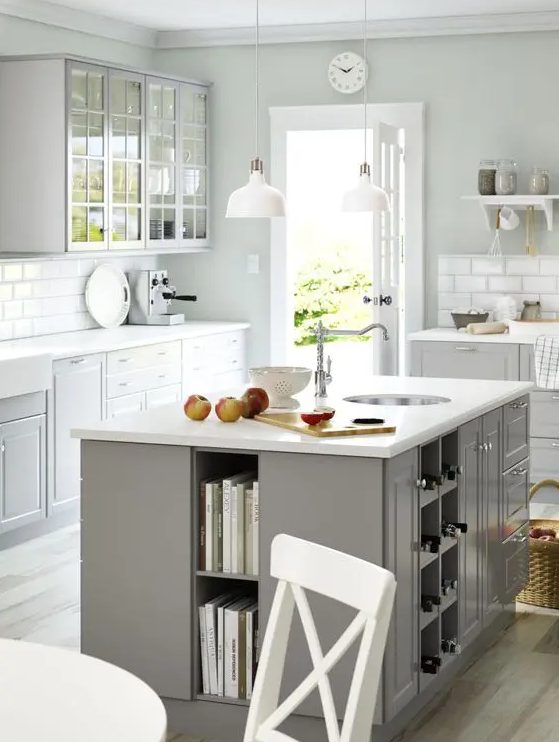 a Scandinavian kitchen with dove grey cabinets, white countertops and a white tile backsplash, a grey kitchen island with open book and wine bottle storage and drawers