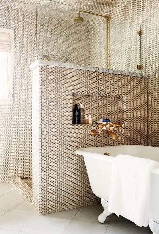 a bathroom clad with penny tiles and with neutral tiles on the floor, brass fixtures and a clawfoot bathtub, a niche for storage