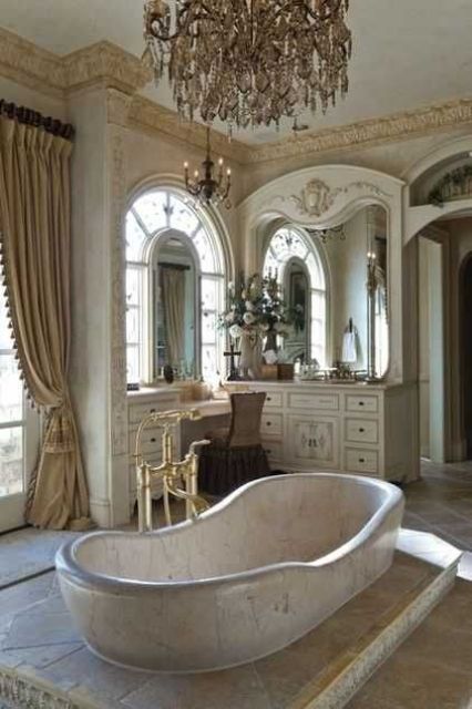 a beautiful French bathroom with a large vanity and a makeup space, large mirrors and a statement crystal chandelier, a built in bathtub and vintage fixtures