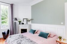 a beautiful and chic French style bedroom with a green accent wall, a bed with blue and teal bedding, a vintage fireplace, a floor lamp and some blooms