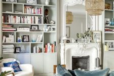 a beautiful and light-filled French chic living room with grey bookcases, a vintage fireplace, a slate blue sofa and some pretty modern chairs