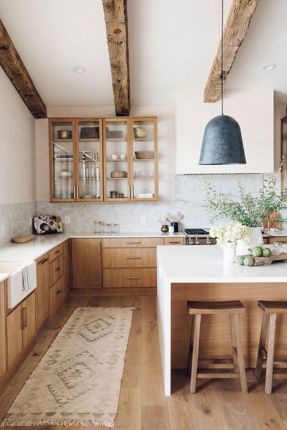 a beautiful and serene kitchen with reclaimed wooden beams, light-stained cabinets, white stone countertops and a black pendant lamp