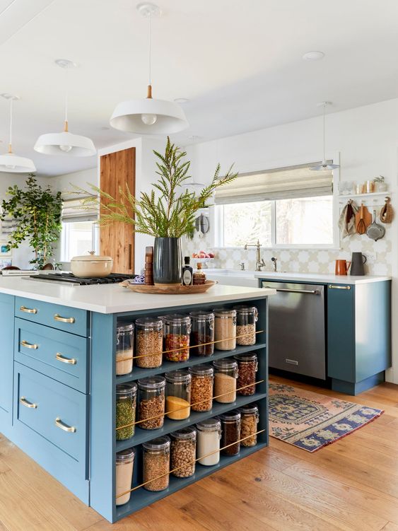 a beautiful blue kitchen with catchy tiles, white stone countertops, a large kitchen island with drawers and open shelves to store various stuff