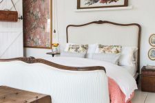 a beautiful cottage bedroom in creamy shades, with a vintage bed with neutral bedding, bold art, a mini table and a stained chest as nightstands