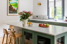 a beautiful kitchen with lower green cabinets, white stone countertops, a catchy kitchen island with glass storage compartments