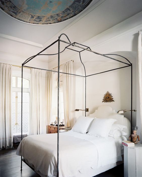 a beautiful neutral bedroom with an accented ceiling, a metal frame bed with neutral bedding, a stained and a painted nightstand