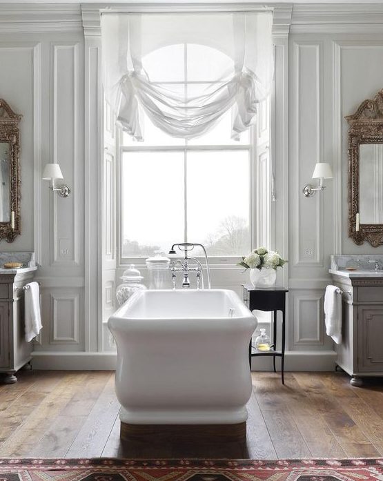a beautiful vintage inspired bathroom with a white tub, curtain, mirrors and chic vanities plus a rug shows off French style at its best