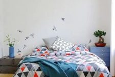 a catchy and pretty bedroom with a light-stained bed with geometric bedding, a navy nightstand with a potted plant and a small shabby chic nightstand with drawers for a catchy look