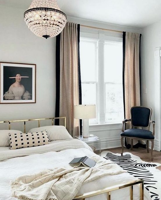 a chic Parisian bedroom with a gold bed, a crystal chandelier, a refined chair and blush and black curtains