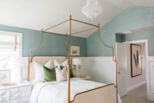 a chic modern bedroom with blue grasscloth wallpaper, a brass frame bed, a white sculptural nightstand and a small side table