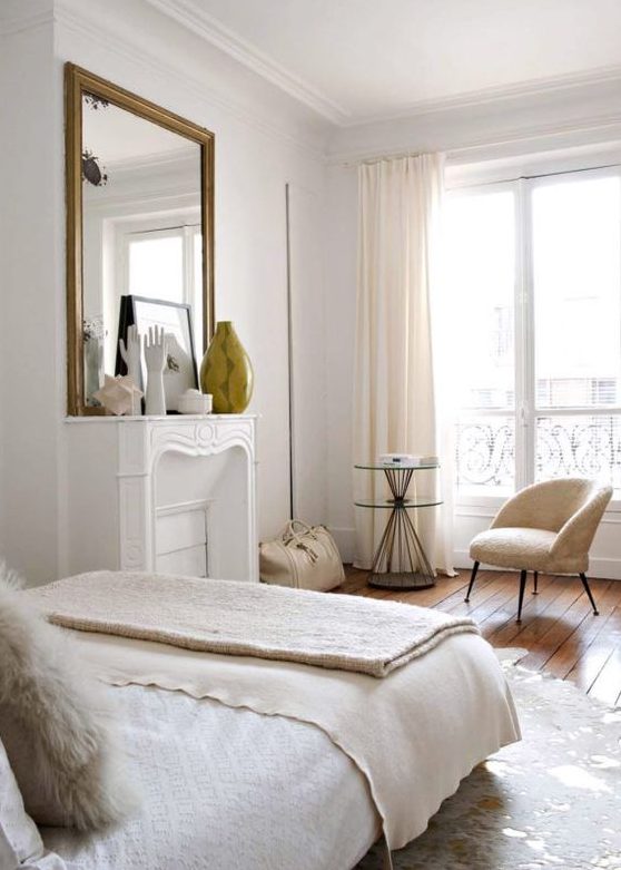 a chic neutral Parisian bedroom with a faux fireplace, a statement mirror, a neutral chair and a large bed