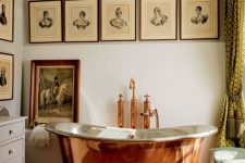 a chic vintage French bathroom with a copper tub, a terracotta tile floor, a gallery wall and grey furniture is wow