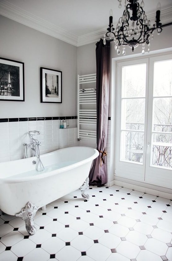 a chic vintage-inspired bathroom with a clawfoot bathtub, purple curtains, a crystal chandelier, artworks and black and white tiles