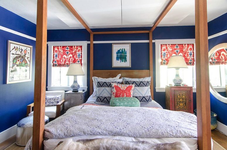 a colorful bedroom with blue walls, a framed bed, bright bedding and blinds, a metal and an oriental cabinet, a chair and a silver pouf