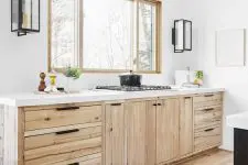 a compact blonde wood kitchen with white stone countertops and black handles plus a contrasting black kitchen island and elegant sconces