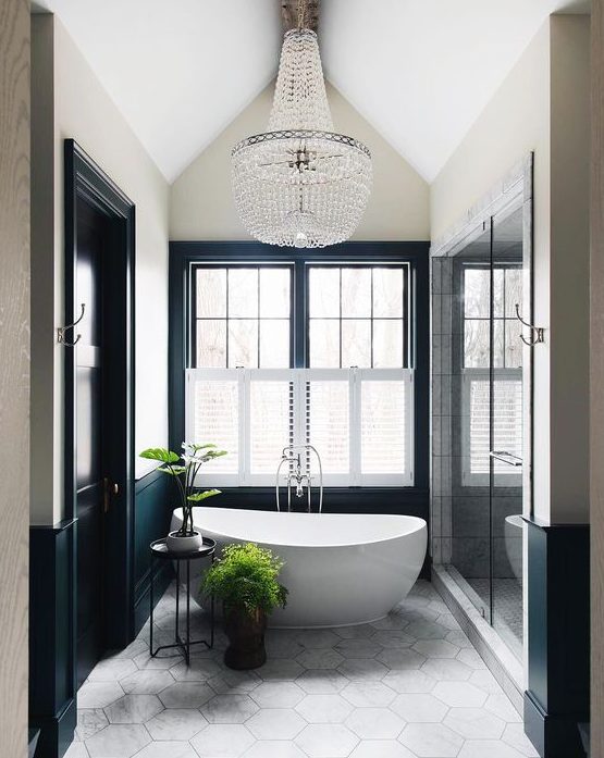 a contemporary French style bathroom with an oval tub, a large crystal chandelier, black and white walls and a hex tile floor